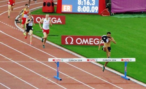 Mahiedine Mekhissi-Benabbad of France clearing the final barrier of the steeplechase at the 2014 European Championships in Athletics. He finished first, but was later disqualified for removing his shirt in the final 100 meters (photo by Jane Monti for Race Results Weekly)